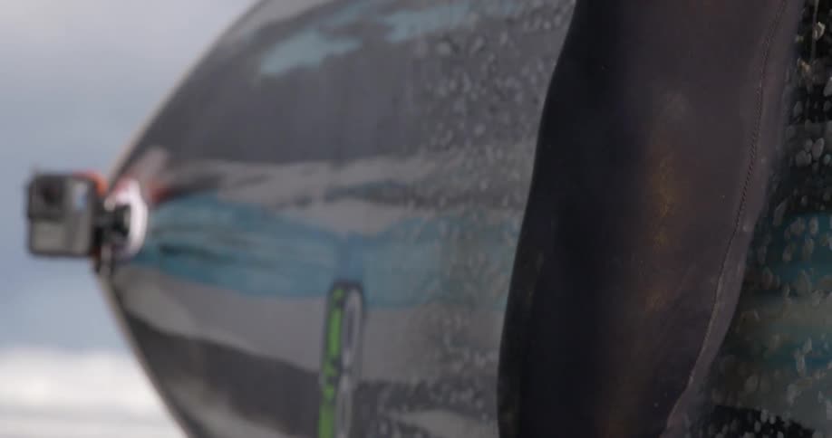 A surfer in a wet suit picking up a surfboard on a sandy beach