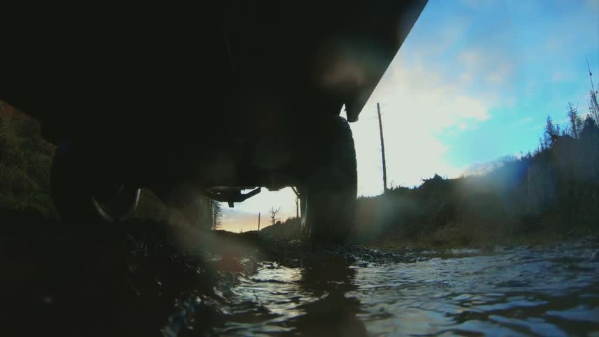 A vehicle driving through a muddy puddle on a dirt road