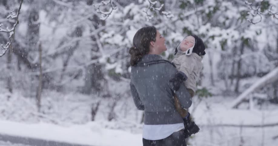 A woman holds her bundled up toddler as they take a walk in the snowfall