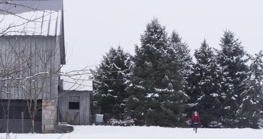 A woman runs across a snowy field in front of a barn