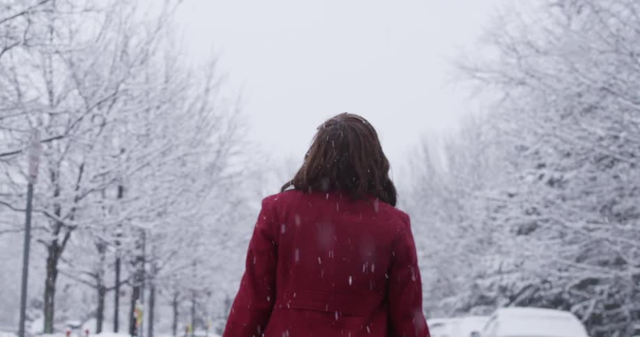 A woman in a red coat walks down a road in the snow
