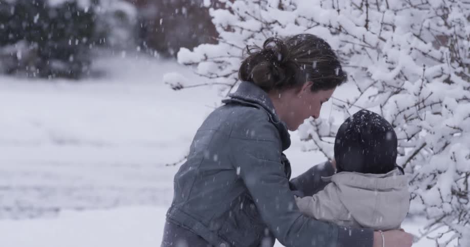 A woman and toddler playing with a tree branch in the snowfall