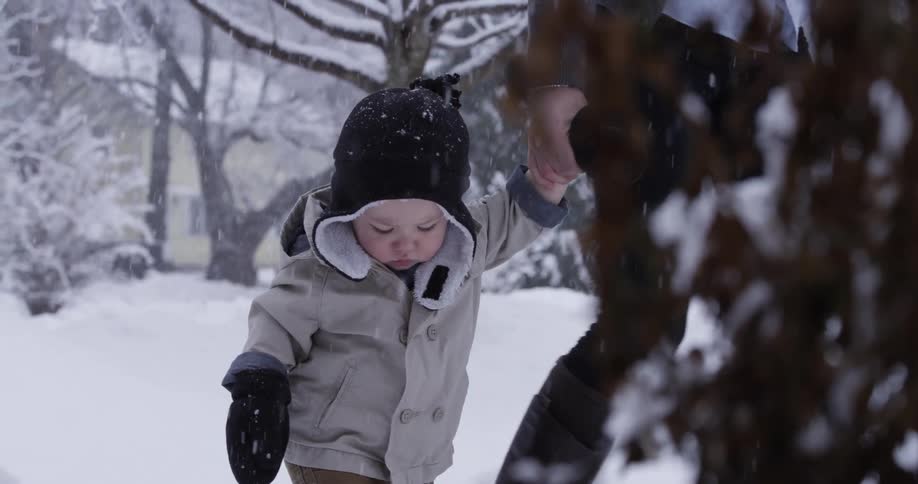 A woman is walking a child outside as it snows