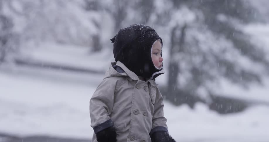 A small child stands outside in the snow
