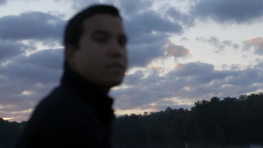 A man is standing by the water looking around at sunset