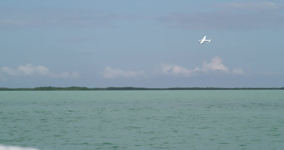 Small white plane flying over the ocean in the distance during the day