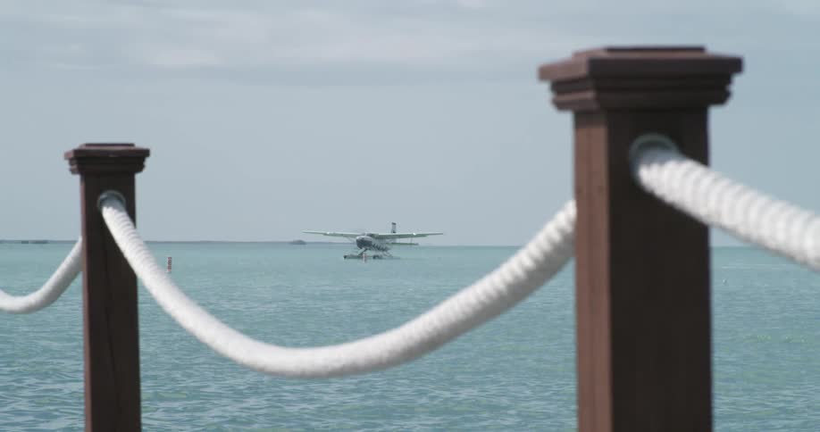 A banister with ropes with an airplane on the ocean with the sky and clouds in the background