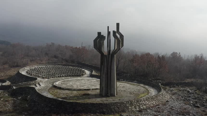 A large stone monument in an open arena setting with outdoor stone seating in a forest on a misty day