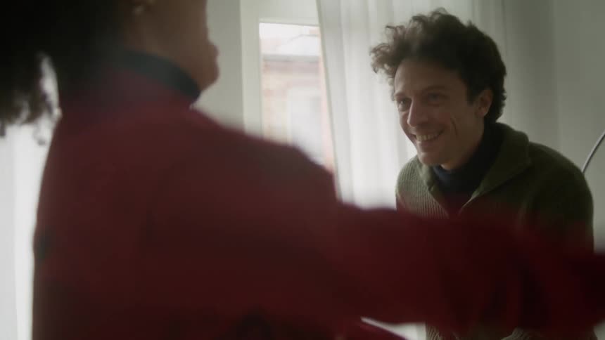 A man and woman laugh as they dance around their apartment