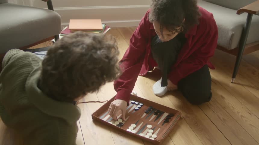 A couple sitting at home in a living room playing backgammon at daytime
