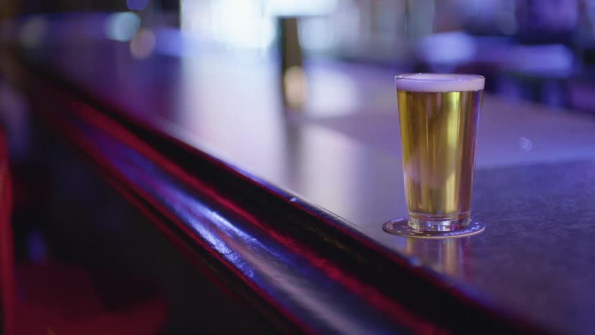 A glass of beer with bubbles on a counter in a bar
