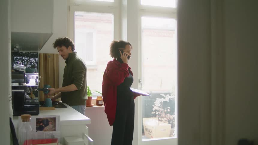 A man washes dishes while a woman talks on the phone