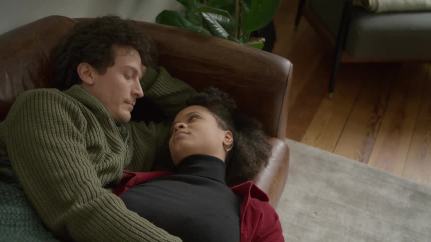 A couple laying down on a sofa in a living room at home staring at each other romatically