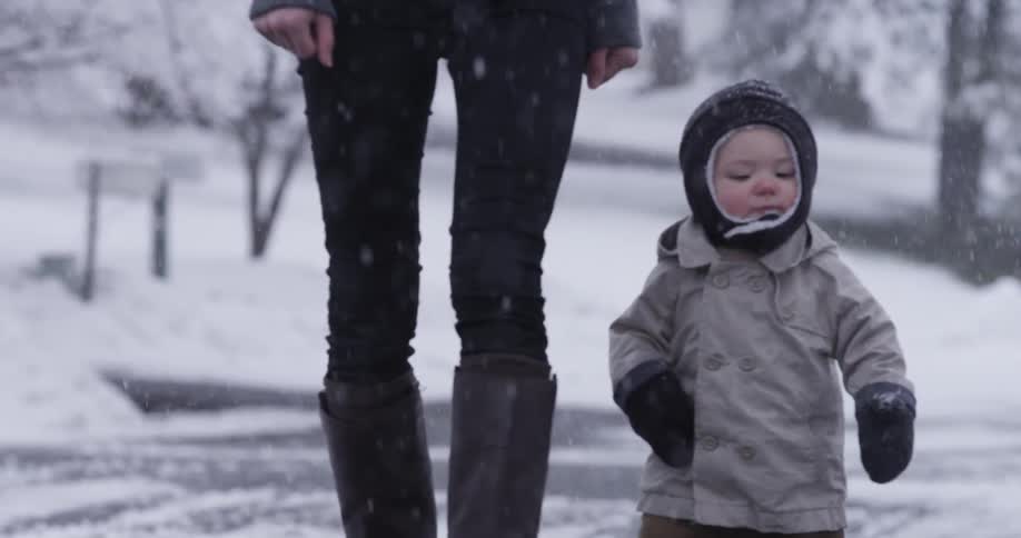 A woman and toddler take a walk during a snowfall