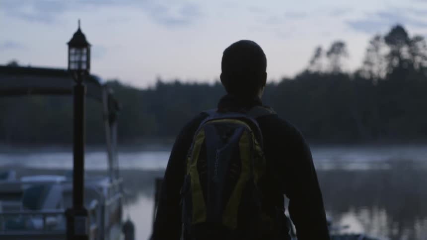 A man wearing a backpack and carrying a fishing pole walks on a pier
