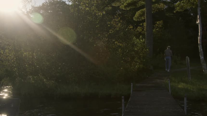 A man walks down a small path with a dock and lake in the foreground