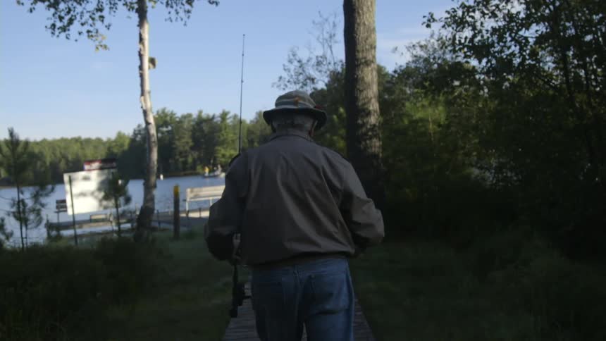 A man is walking towards the water with a fishing pole