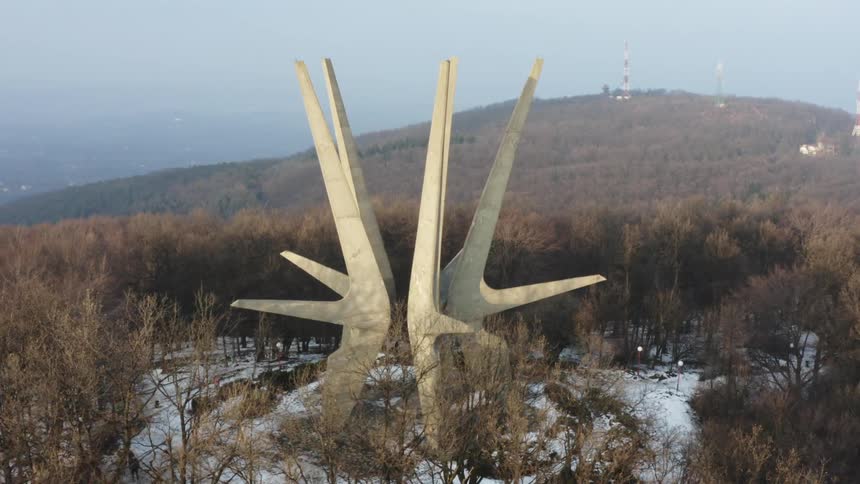 A large architectural sculpture sits at the bottom of a hill near lighthouses