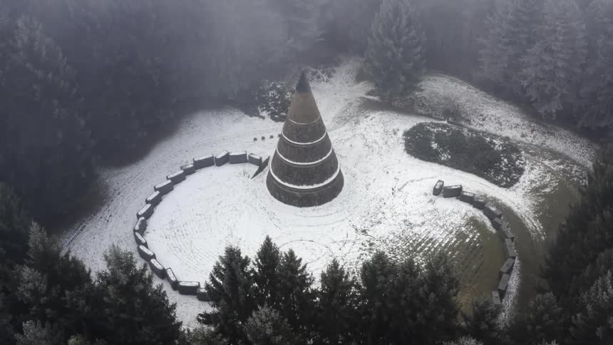 Aerial view of a conical monument in the snow covered clearing in the forest