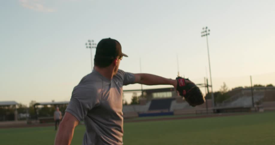 A man in a baseball field catching and throwing a baseball with the sky and clouds in the background