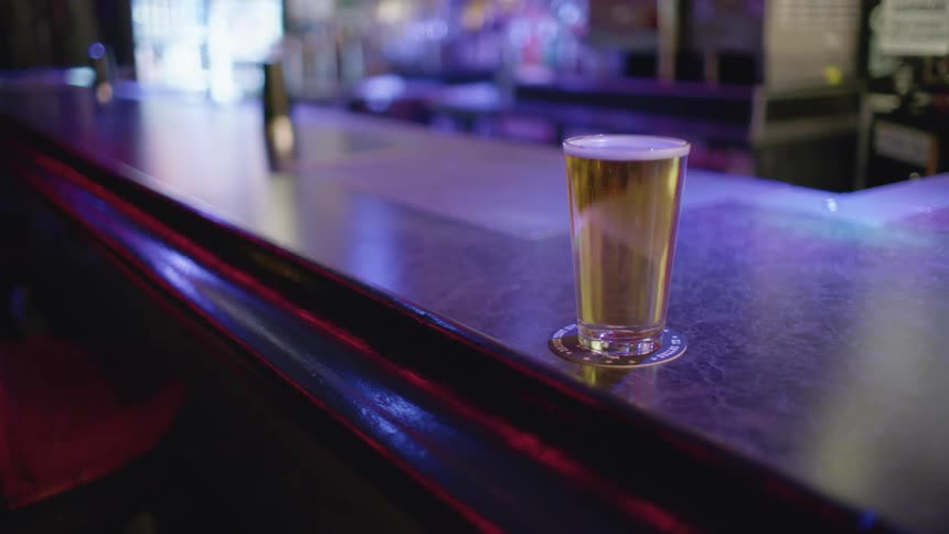 A glass full of beer over a coaster over an empty bar counter on a pub