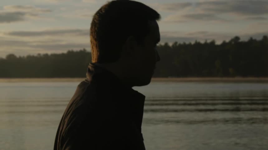 A man is walking near a like at sunset