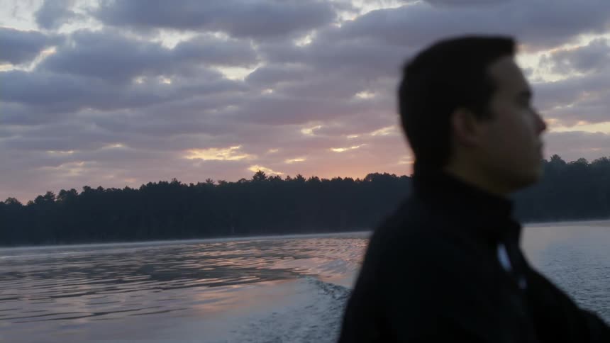 Man rides on a boat across a lake at sunset