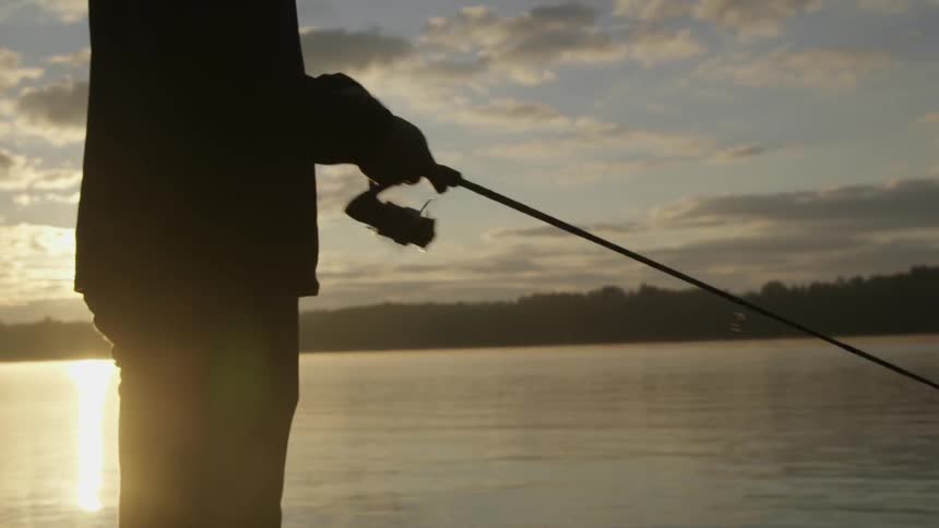 A man is fishing in the water at sunset