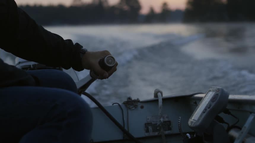 A man resting his hand on the steering handle of an outboard engine as he travels across water