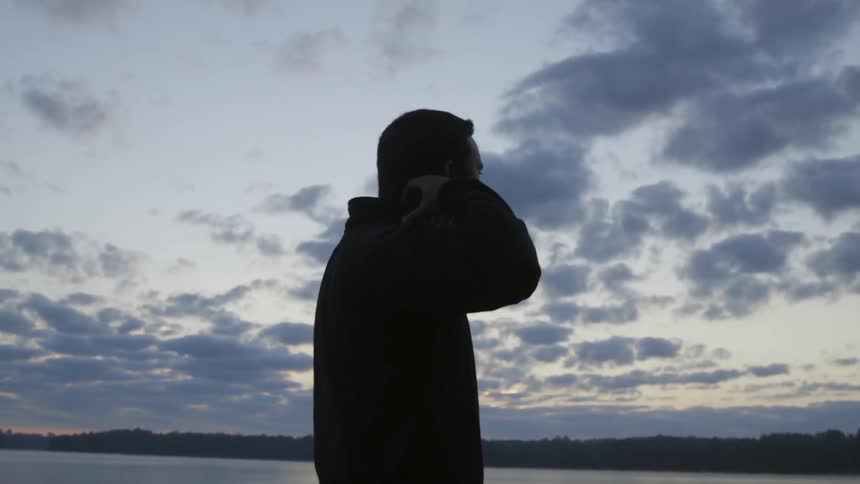 A silhouetted man stands in front of a lake at dusk