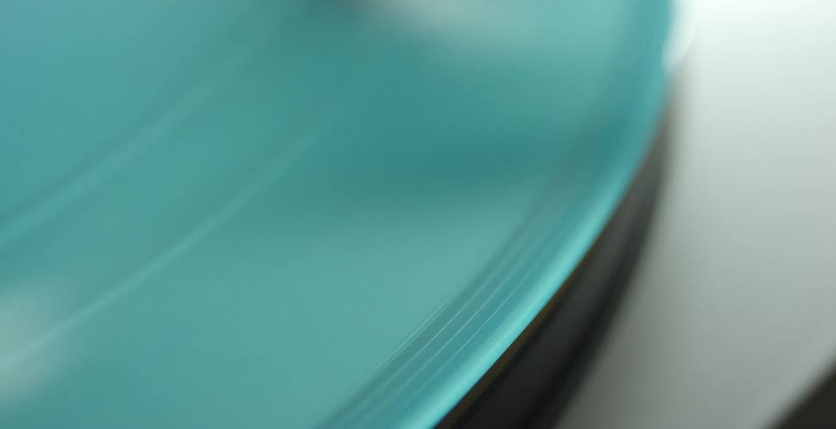A blue green curve spinning with grooves and light reflecting off of it