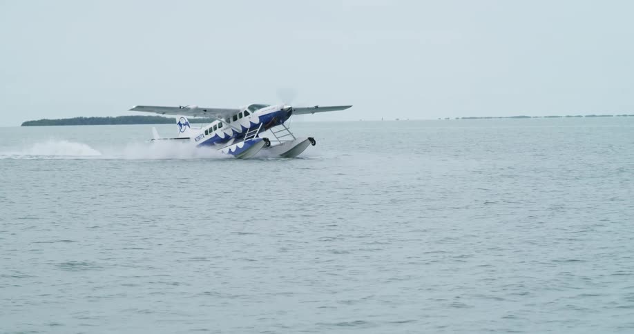 A sea plane leaves a wake as it lands on the water on a gray day