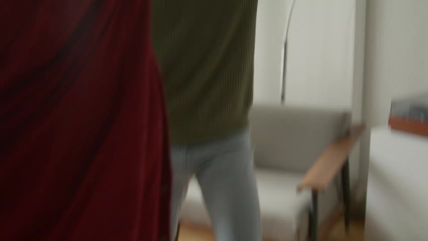 Man with green sweatshirt and jeans and woman wearing red shirt and black pants dance in the living room at home