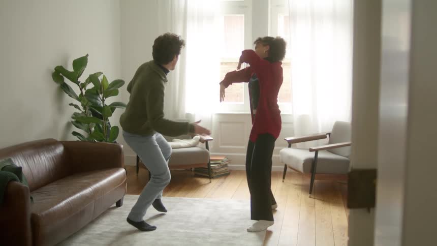 A man and woman smile as they dance around their apartment living room