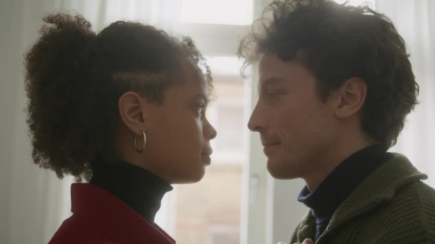 Woman with curly hair black turtle neck sweater and man with green sweater lovingly look into each others eyes