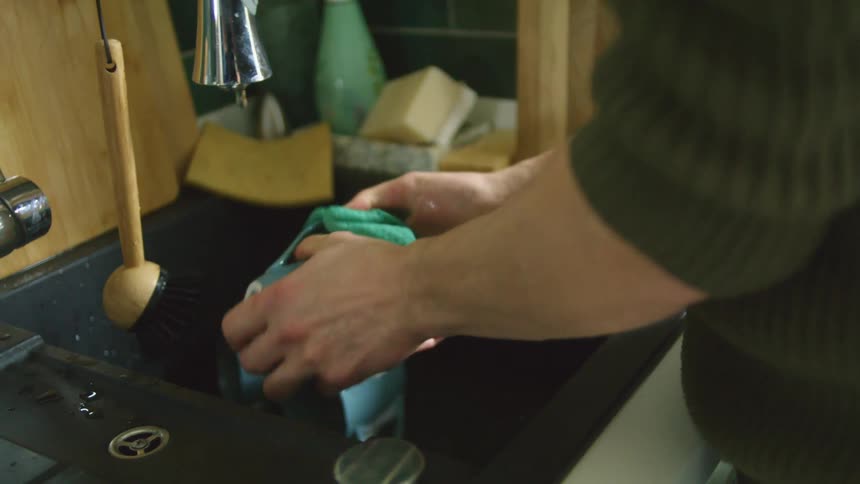 Man with green sweater does the dishes in the kitchen