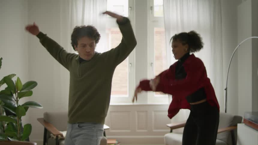 A couple dancing around at home in their living room playfully during the day time