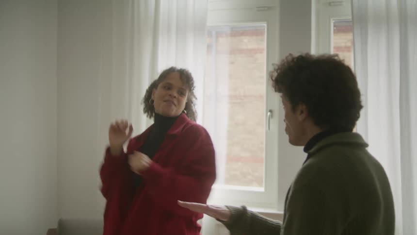 A man and a woman dancing around together happily in a living next to a window at daytime