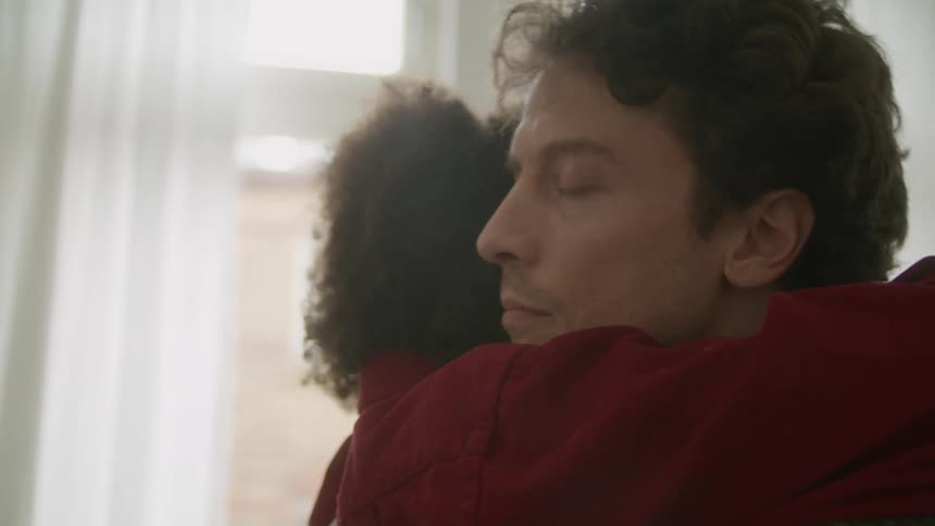 A man and woman touching foreheads go in for a hug as they stand in front of a window