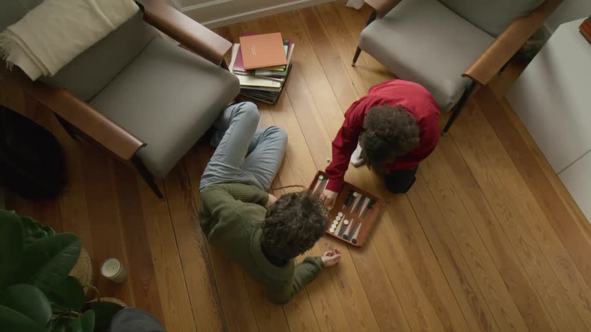 Man wearing green sweater and woman with red shirt play backgammon on the floor in the living room