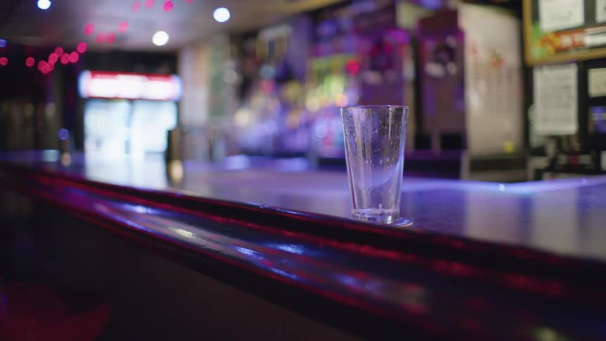 An empty glass with droplets on a counter in a bar
