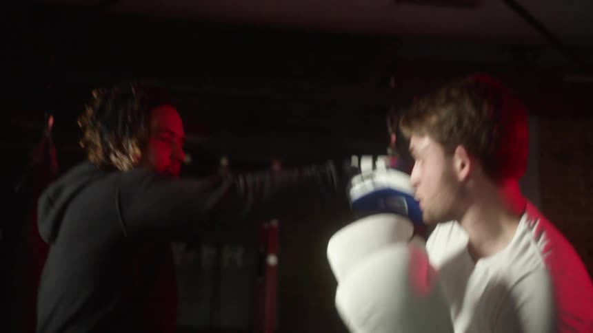 Male boxer with white shirt trains with the coach in the boxing gym