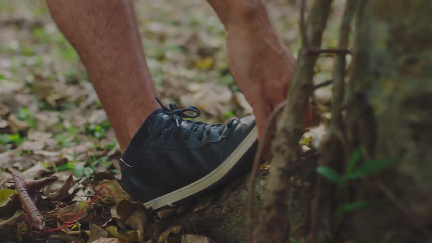 Man wearing black shoes warms up his leg before workout in the park