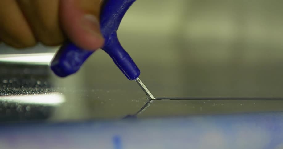 A person turning a tool to tighten a nut on a slit in a metallic surface