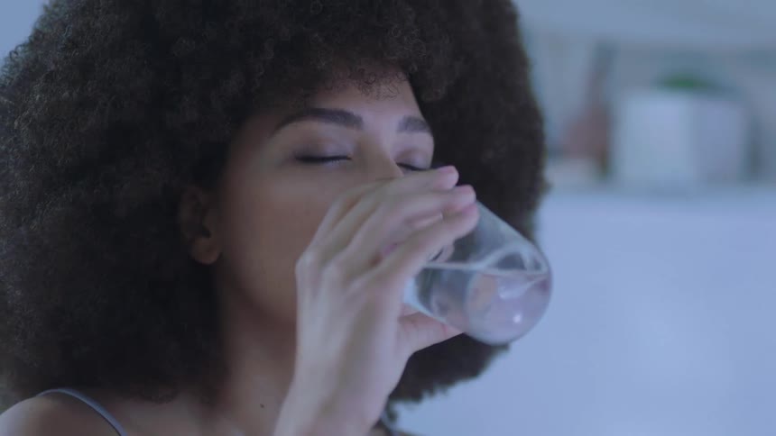 Brunette woman with frizzy hair closes her eyes and drinks a glass of water