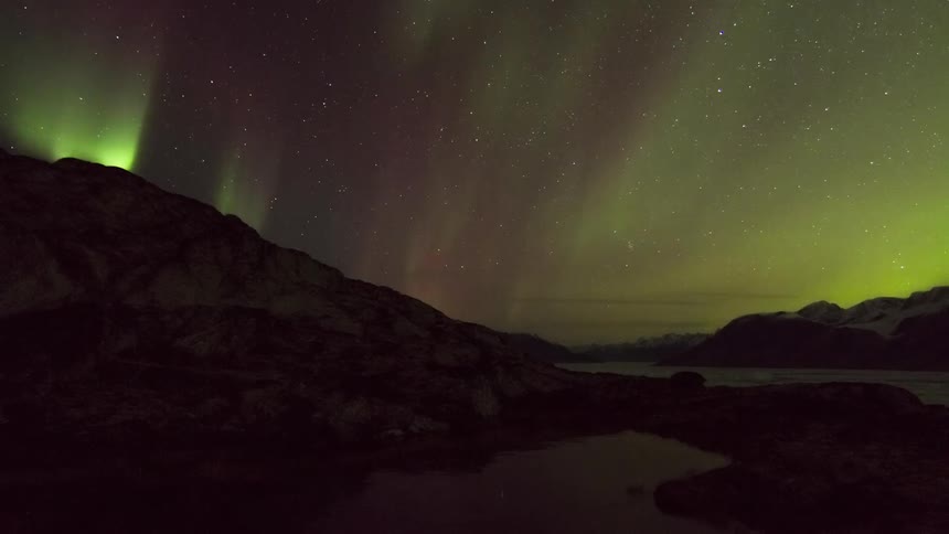 Aurora borealis shining brightly in a star filled sky above snow covered mountains and lake