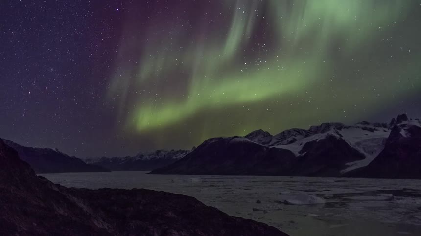 Aurora borealis shining brightly in a star filled sky above snow covered mountains and ice covered lake