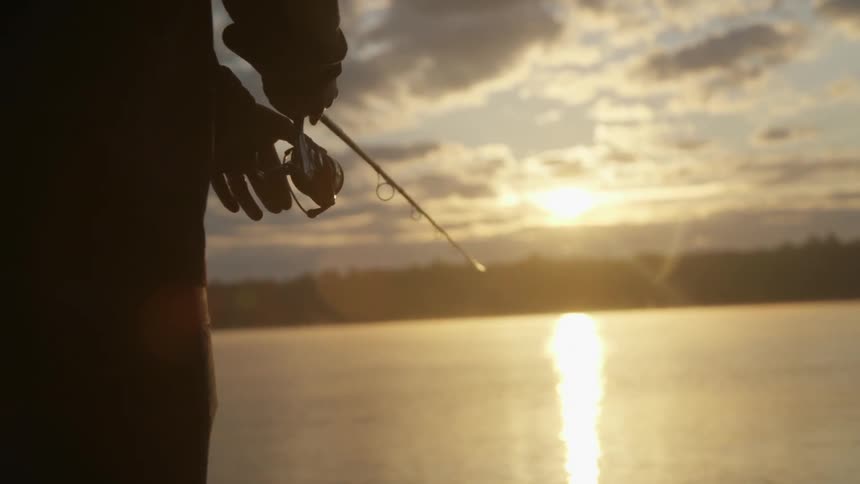 A fisherman casts a line and reels it back at dusk or dawn