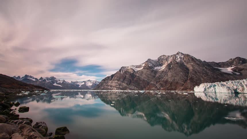 Reflection of the sky and passing clouds on a lake surrounded by mountains