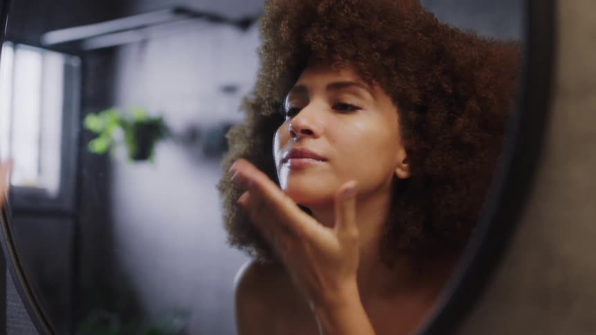 A young woman washes her face in a mirror during the day